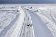 Bird's eye view of a white car on the snow-covered Ring Road (Route 1) surrounded by white winter landscape in Iceland
