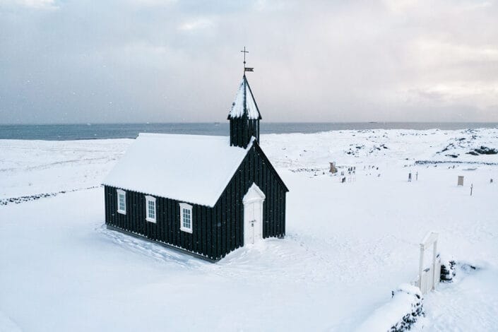 Black Budakirkja church and its churchyard covered in snow, seen from above