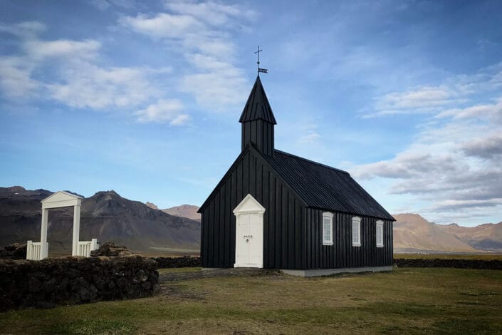 Black Budakirkja church with the white churchyard gate, mountains in the background