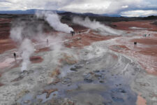 Several steaming fumaroles on the red-brown clay of Namafjall Hverir, with visitors walking between them