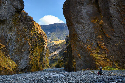 A hiker sitting at the foot of the huge rock walls in the narrow part of Stakkholtsgjá