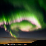 Vivid spiral multicolour aurora borealis lighting up the sky over a road on Iceland's south shore