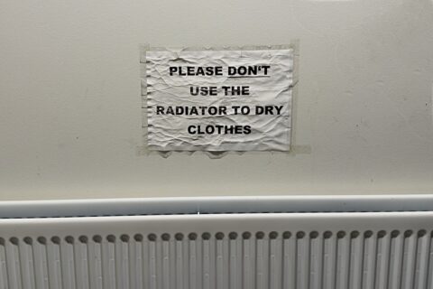 Worn paper sign on a wall radiator in Vík Iceland reading "please don't use the radiator to dry clothes"