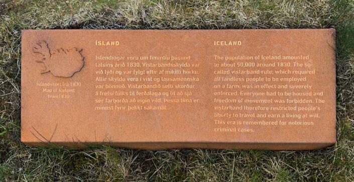 Zardzewiała stalowa tablica z nagłówkiem ICELAND leżąca w trawie przy ścieżce w Thristapar, z tekstem po islandzku i angielsku oraz małą mapą Islandii z 1830 roku